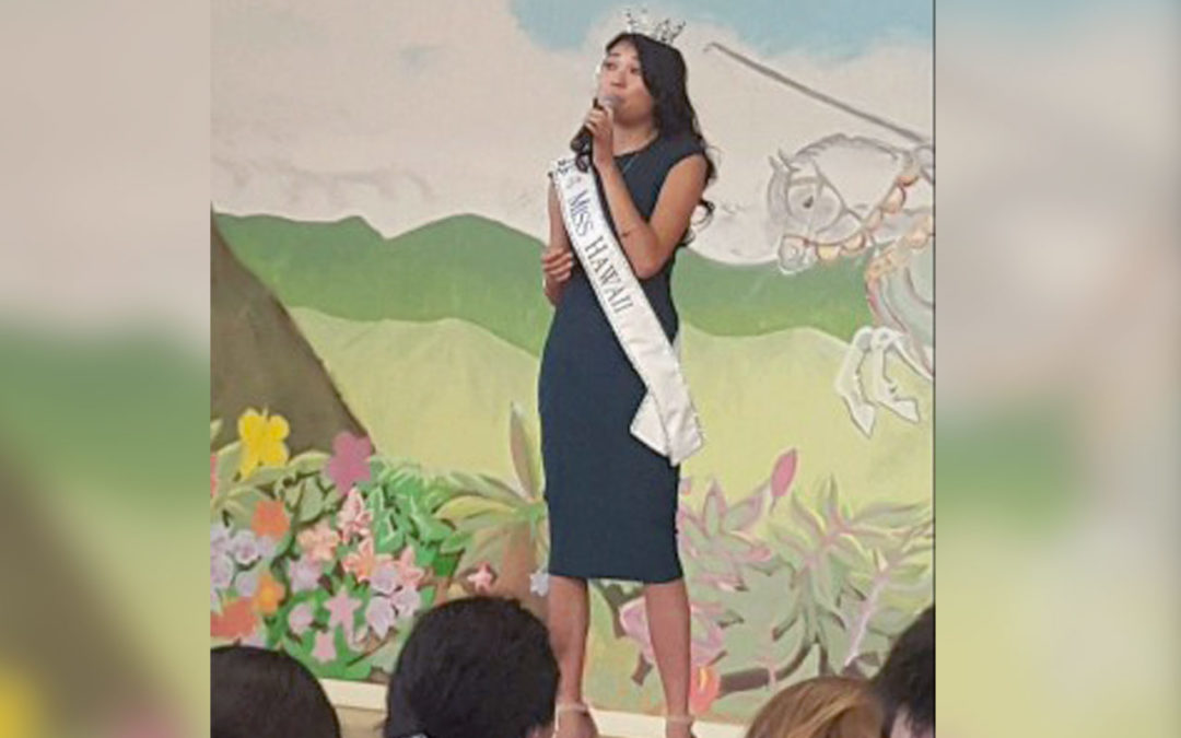 Miss Hawaii standing on stage singing to students
