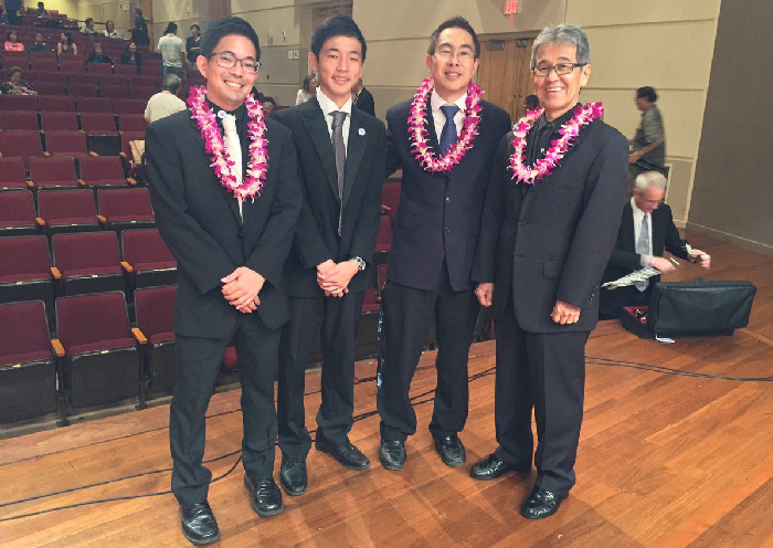 Four adults in black suits wearing orchid lei
