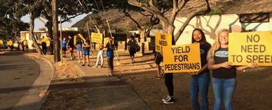 Students and staff hold yellow signs yield for pedestrians, no need for speed