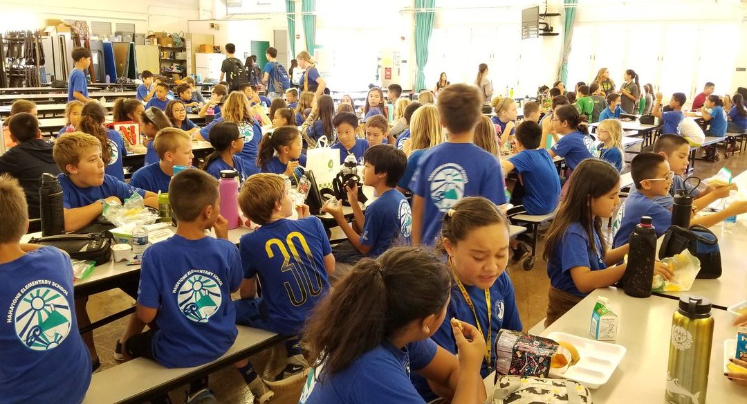 Students from Hahaione Elementary school in blue shirts eat lunch in the cafeteria