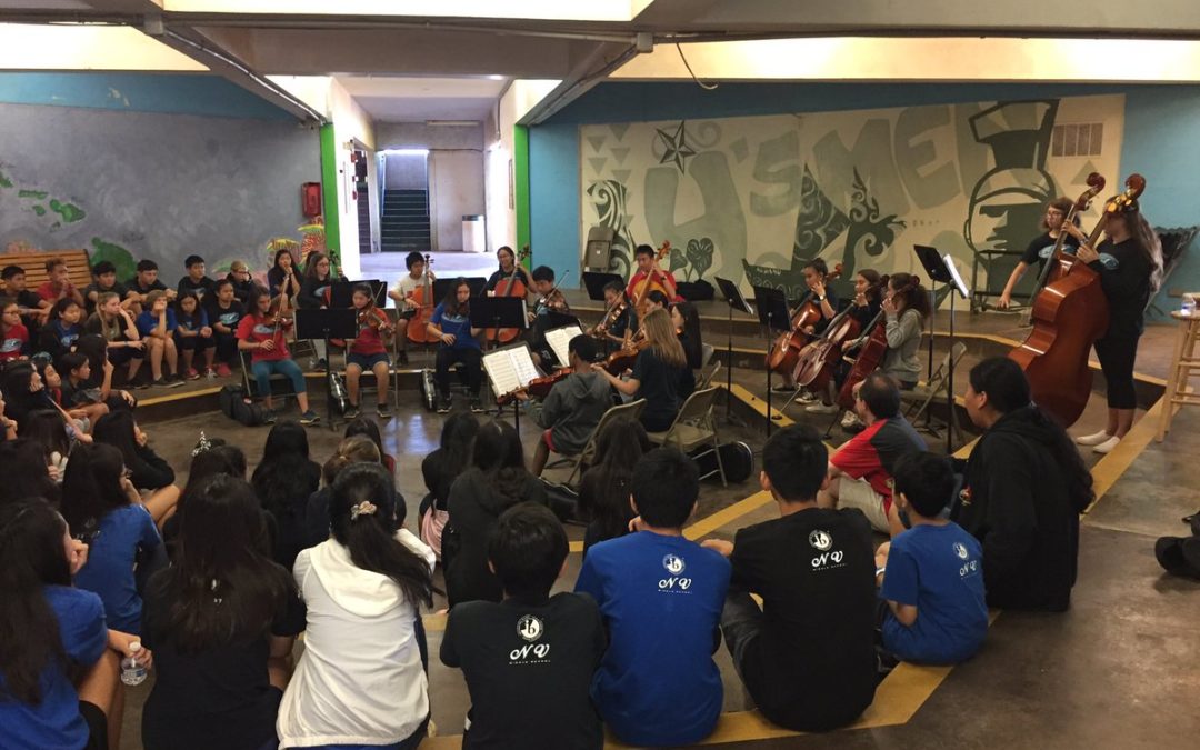Orchestra students play while other students sit around amphitheater