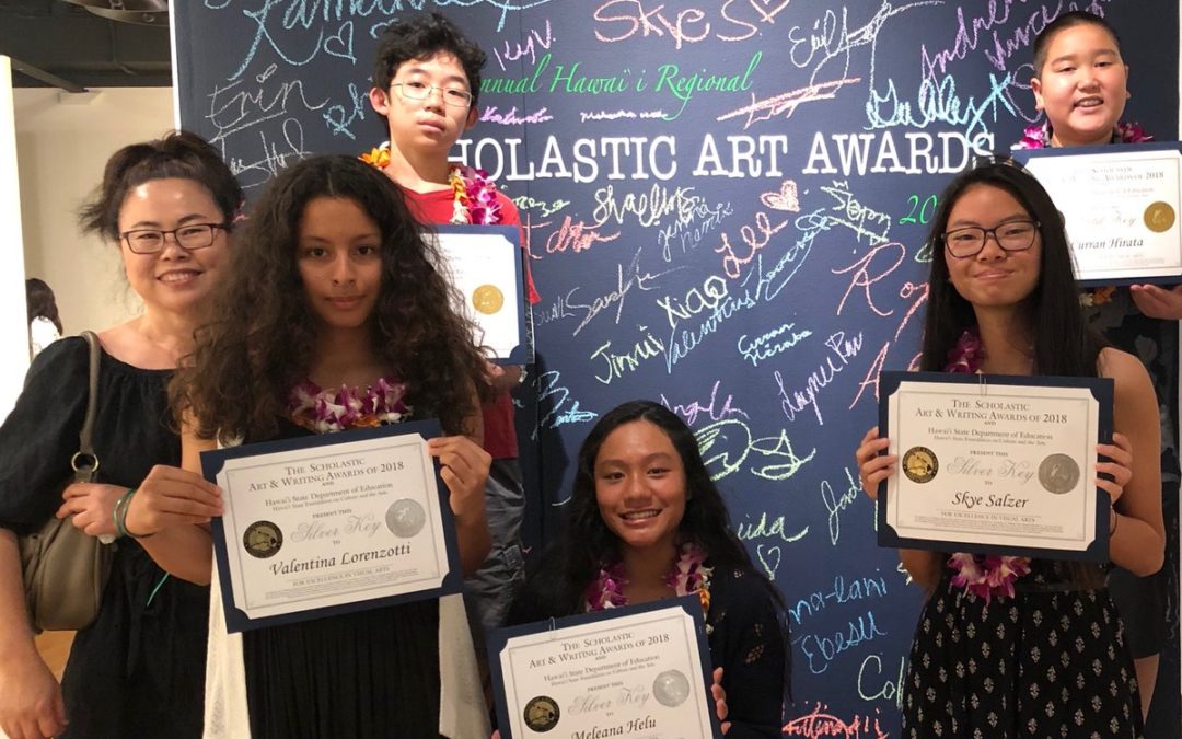 Teacher and five art students holding award certificates in front of chalk writing backdrop for Scholastic Art Awards