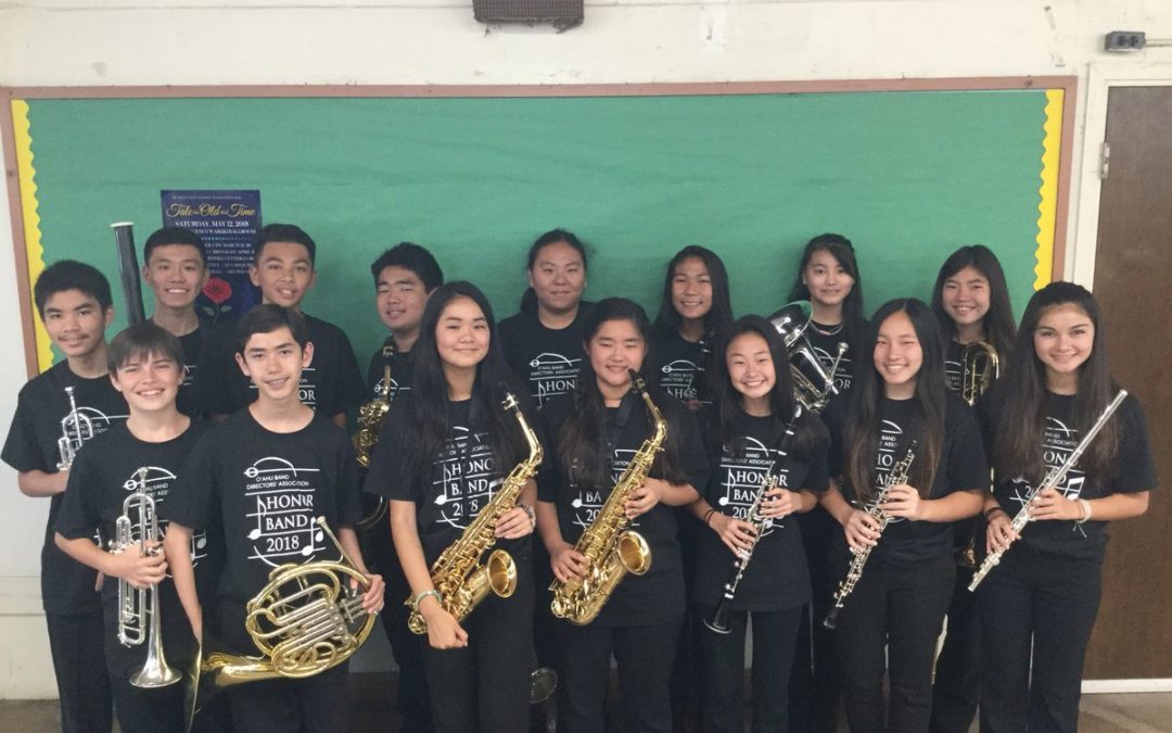 Honor band students in black shirts hold instruments in front of green bulletin board