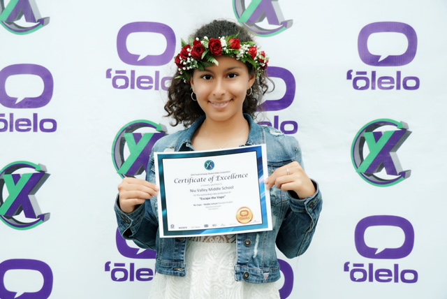 Girl wearing haku lei holds certificate of excellence in front of Olelo Youth Exchange background