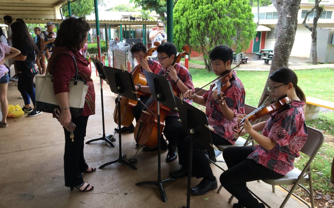 Woman stands and listens near 4 student-orchestra ensemble playing on walkway