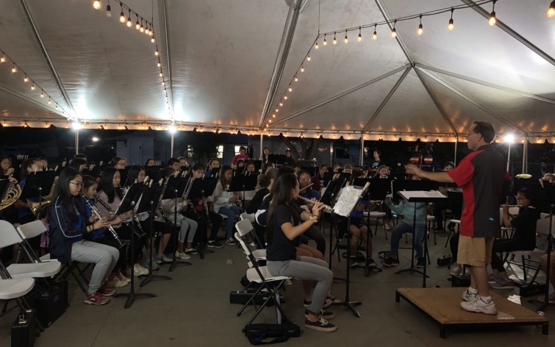 Group of band students rehearsing under a tent with lights