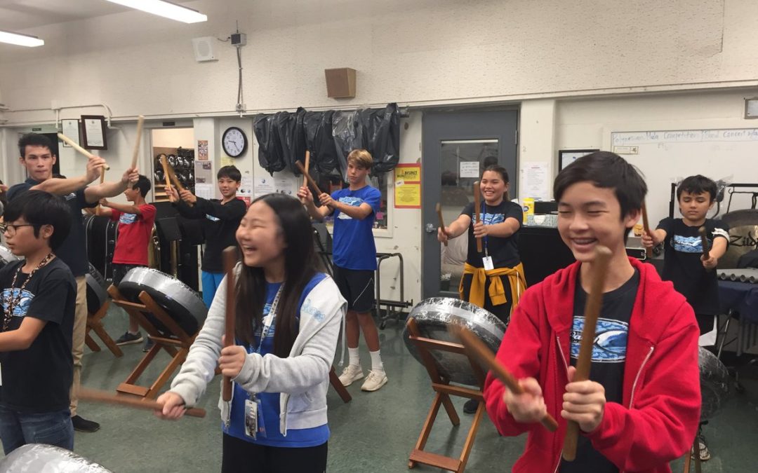 Students in music room smiling and holding taiko drumsticks