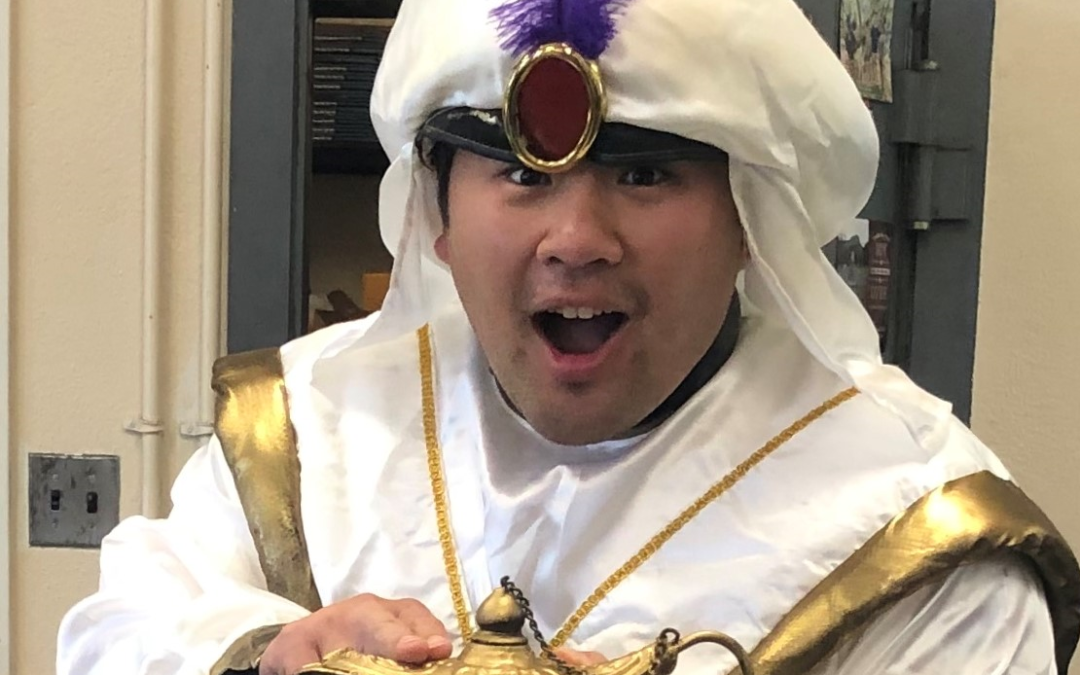 Teacher in white Aladdin costume holding a genie's bottle