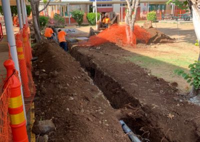 Two construction workers stand in dirt trench to bury power line conduit