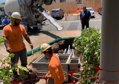 Construction workers bury conduit in trench; cement truck in background