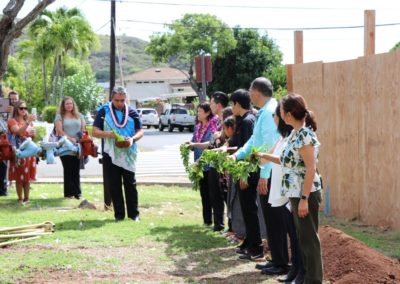 Kahu Davis Begins the Blessing at Groundbreaking with eight people holding a maile lei and onlookers taking photos