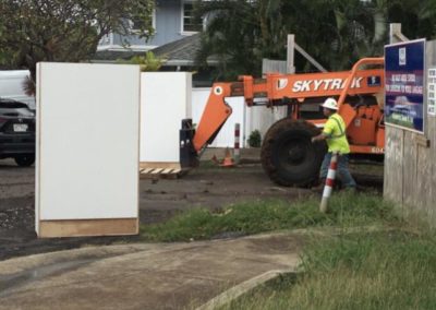 White cabinets in driveway; orange lift truck and construction worker walking.