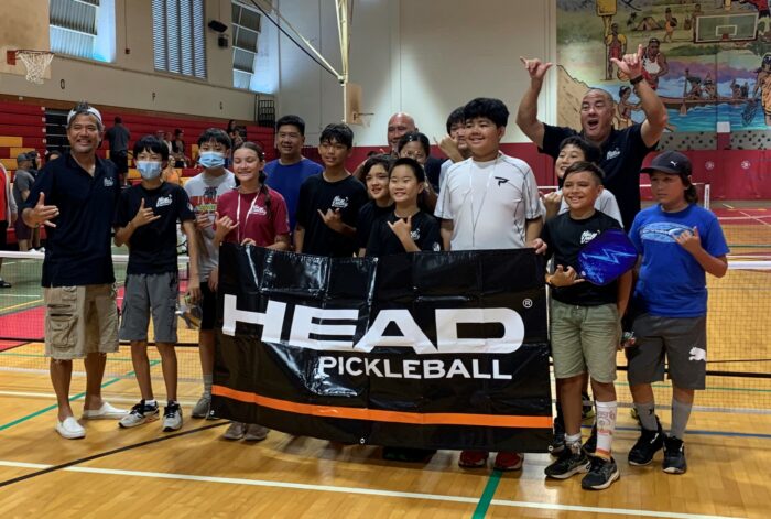 Group of students and adults holding a "Head Pickleball" sign and flashing shakas